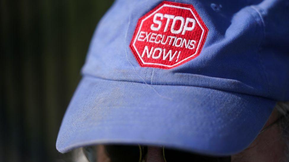 Blue baseball cap protester with STOP EXECUTIONS NOW