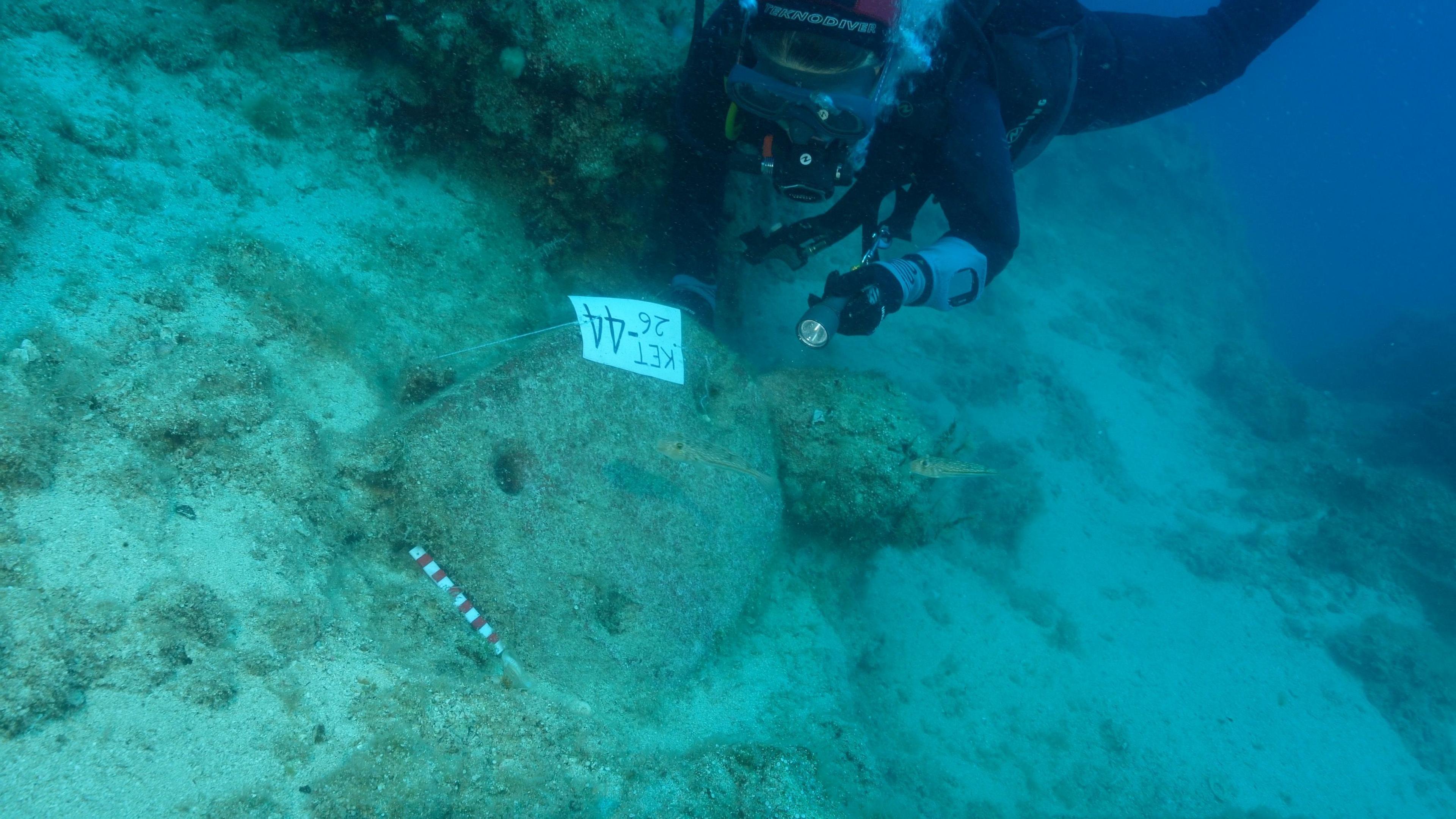 Underwater photograph of the shipwreck site, showing scattered amphorae and stone anchors