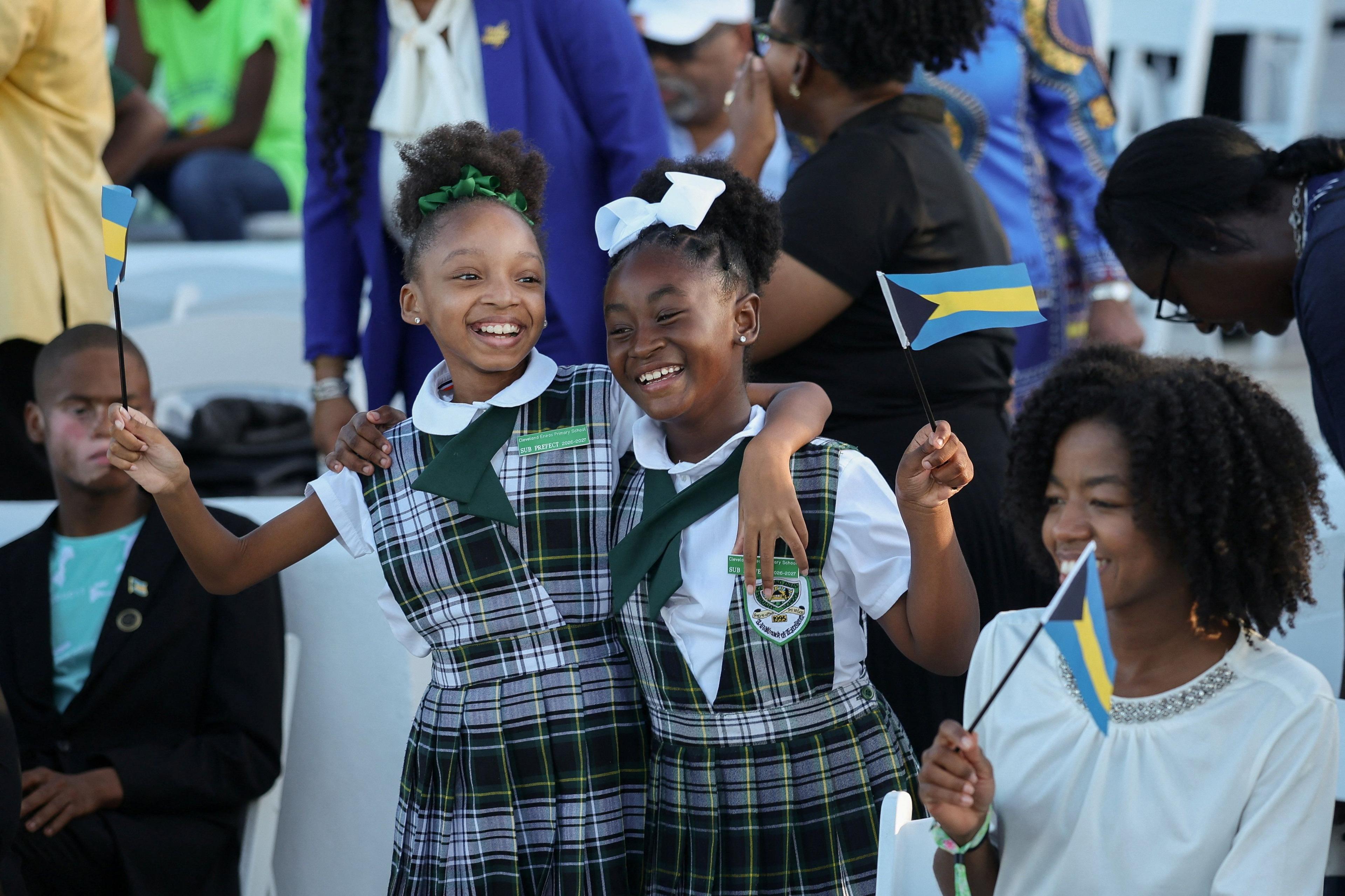 Primary students smile and hold flags of the Bahamas ahead of a youth rally with Britain's King Charles at Clifford Park