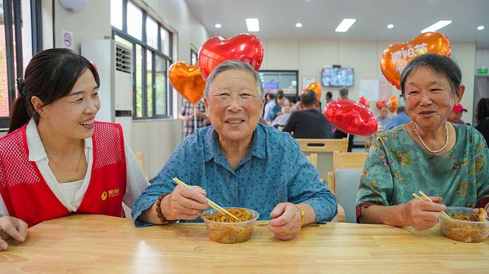 Elderly residents taste longevity noodles while volunteers accompany them at a community care centre during the Double Ninth Festival